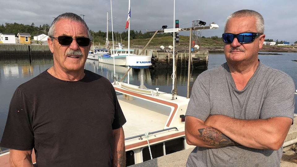 Two men standing on a pier in front of the moored boats.