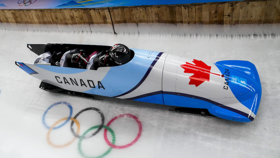 Four Canadian athletes sit in a bobsled race on the track.