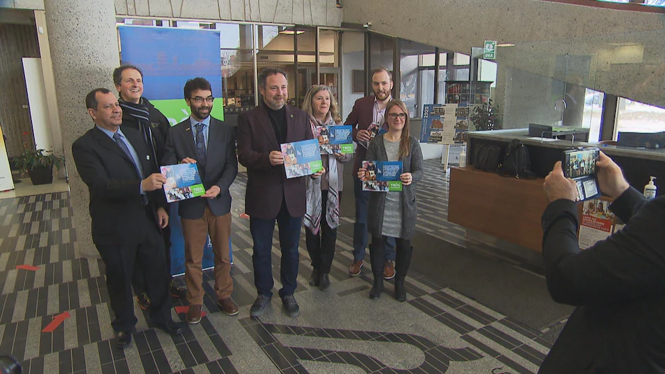 Seven people stand in front of the camera with a plan of action in hand.